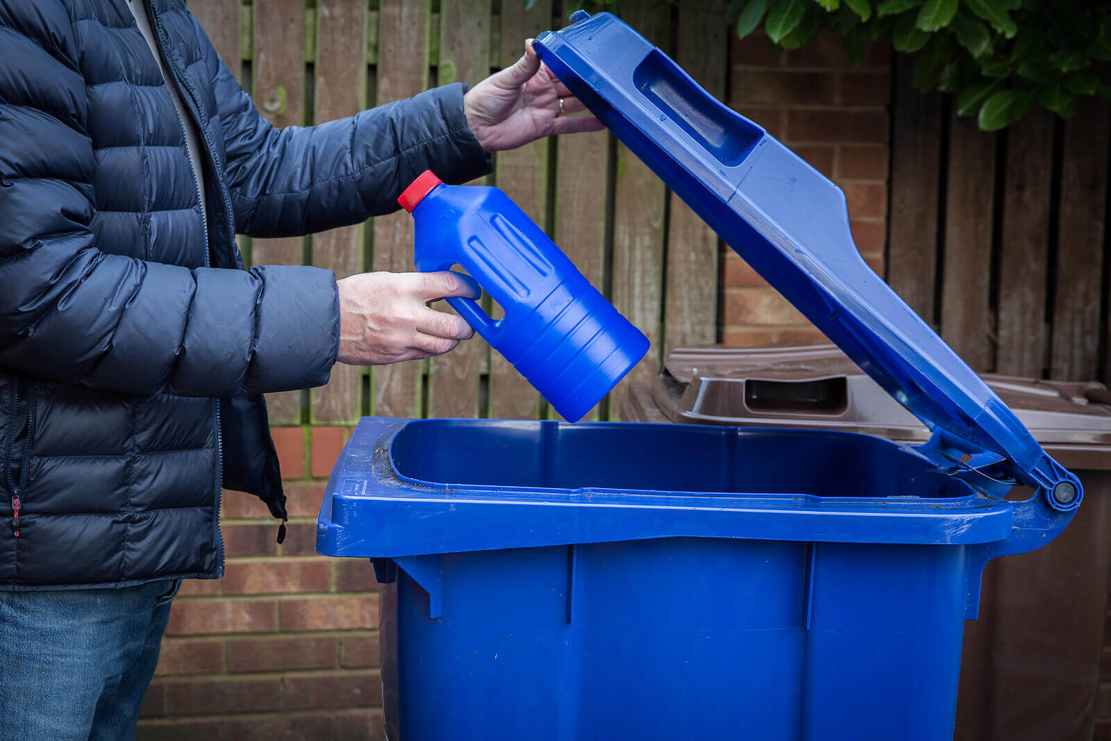 A man recycling a plastic bottle in a wheelie bin